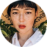 Woman with short hair and freckles wearing a straw hat, surrounded by greenery, representing a vibrant lifestyle, possibly related to travel and adventure.